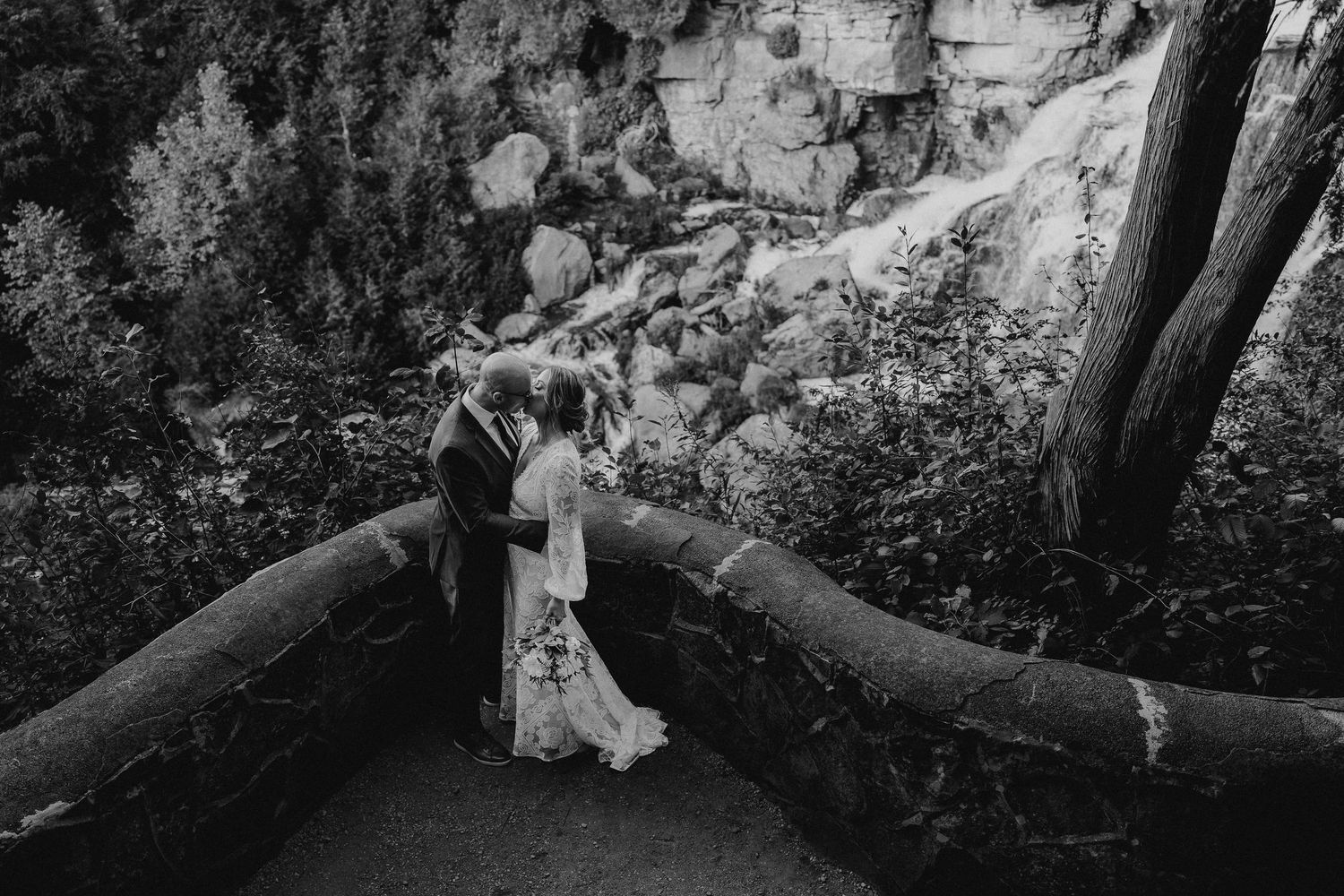 black and white of couple kissing by curved walkway at Inglis Falls, Ontario
