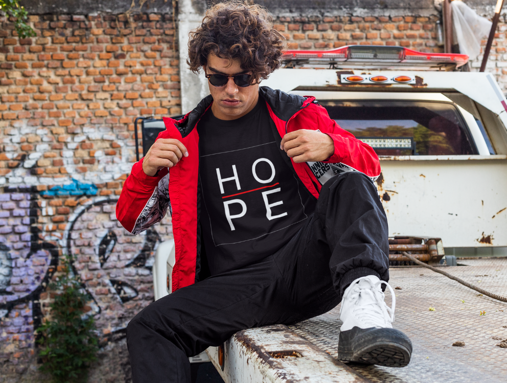 Street fashion photo of someone wearing a black HOPE t-shirt and red jacket against graffiti wall.