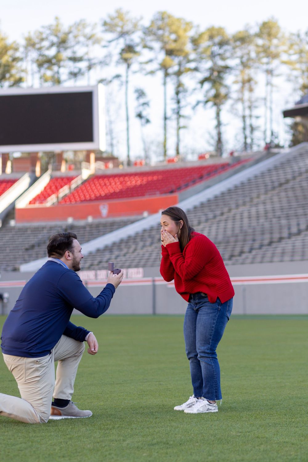 A women in a red sweater gets engaged at a college football stadium proposal.