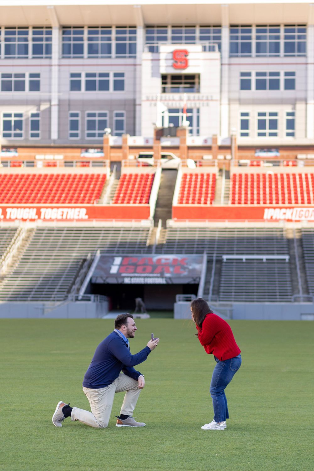A man is on one knee proposing to his girlfriend in a red sweater.