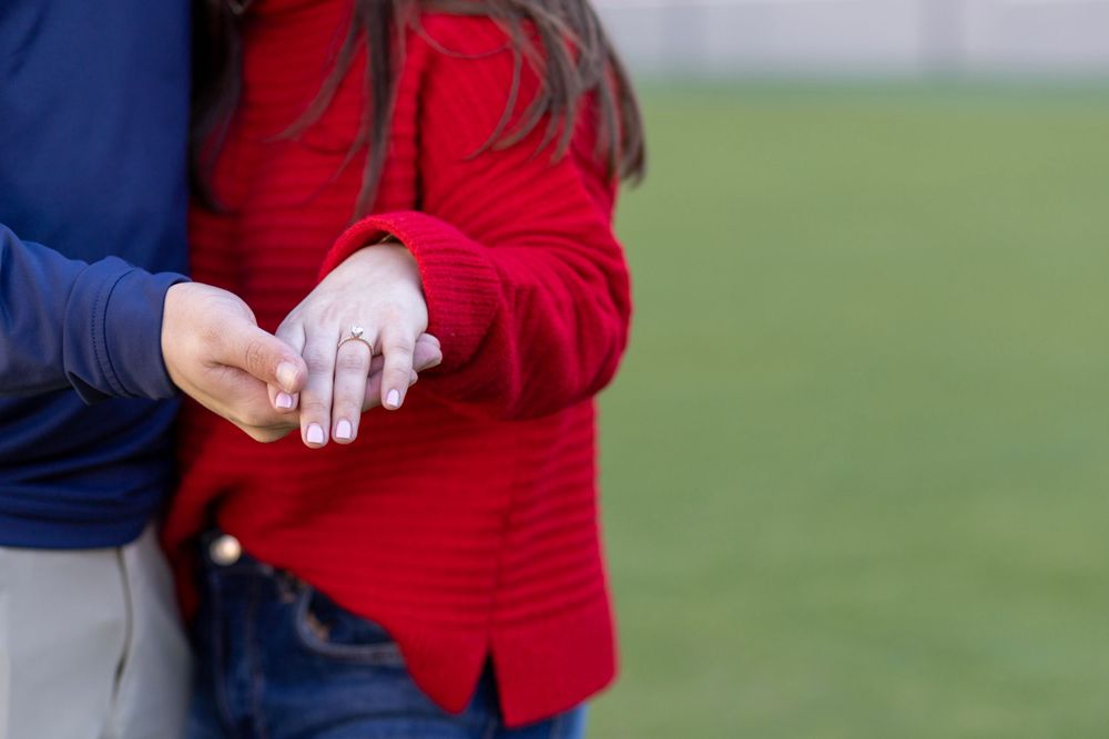 A close up of an engagement ring being worn by a women in a red sweater.