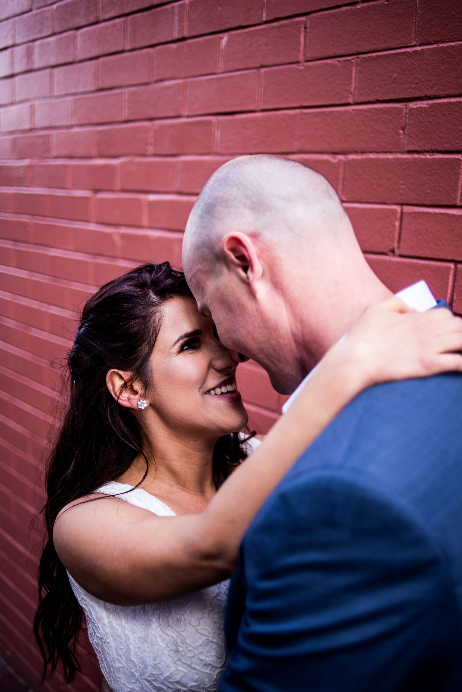 A romantic wedding moment captured against a red brick wall in intimate lighting.