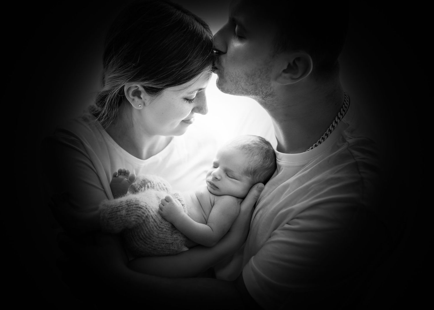 Intimate black and white portrait of tender newborn moment in soft light.