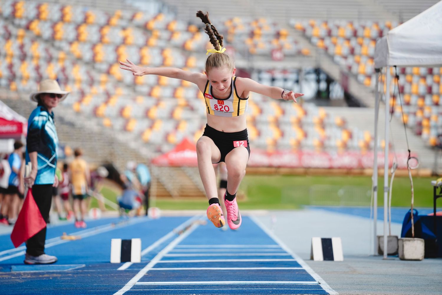 Track athlete mid-jump during long jump competition at outdoor stadium.