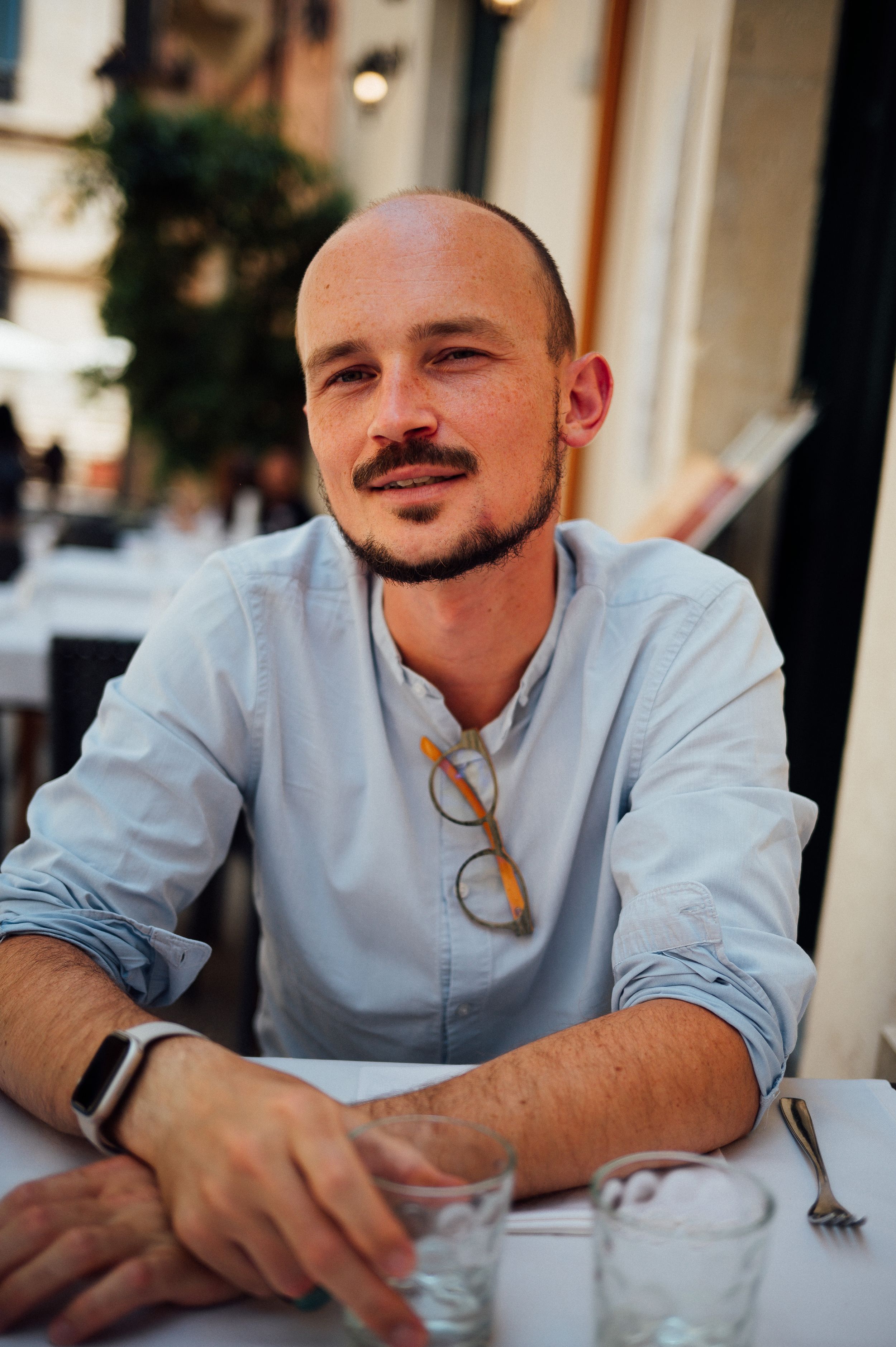 Person enjoying a casual outdoor dining experience wearing a light blue shirt and glasses.