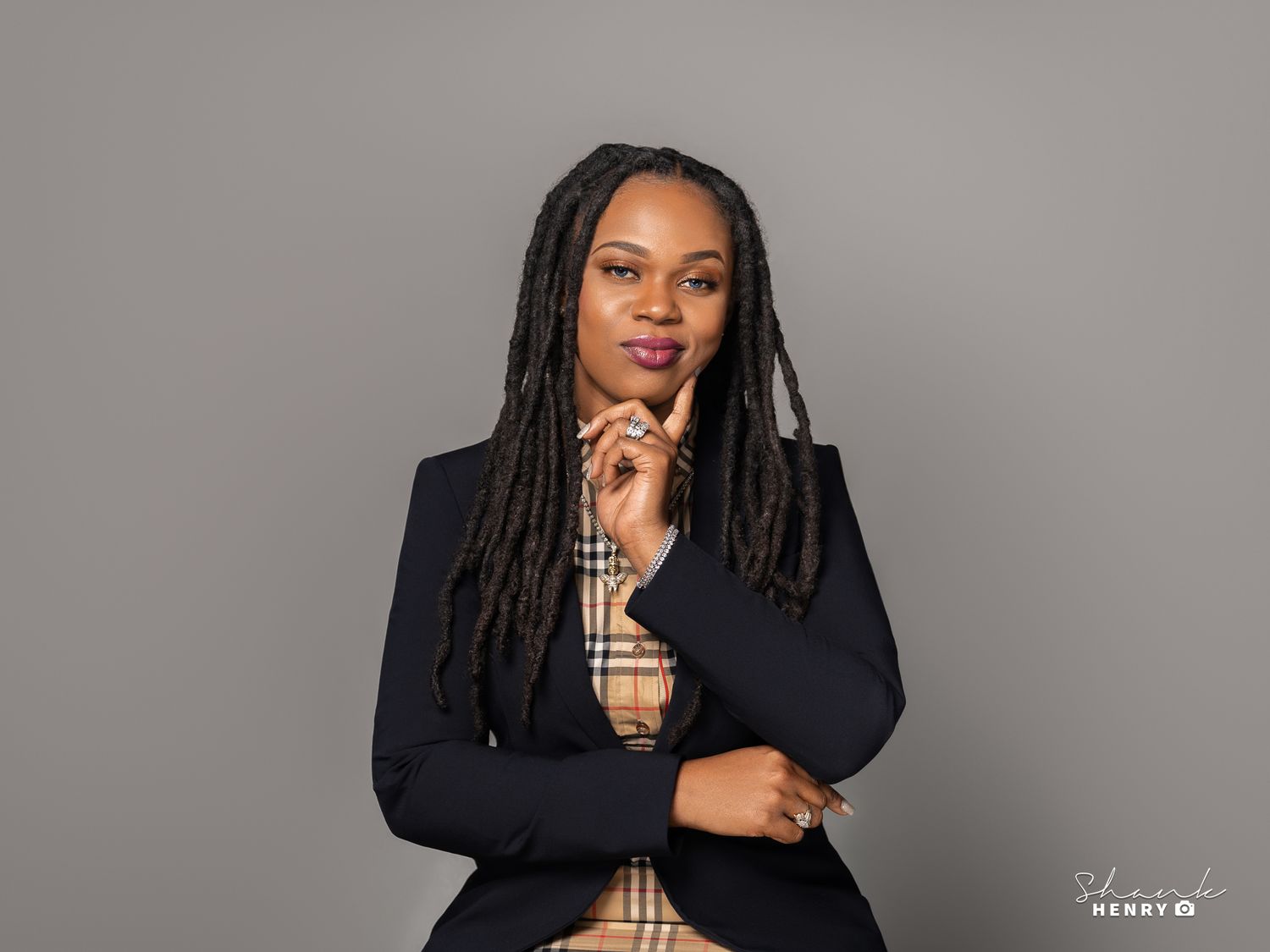 Professional portrait of woman in navy blazer and plaid shirt with hand on chin.