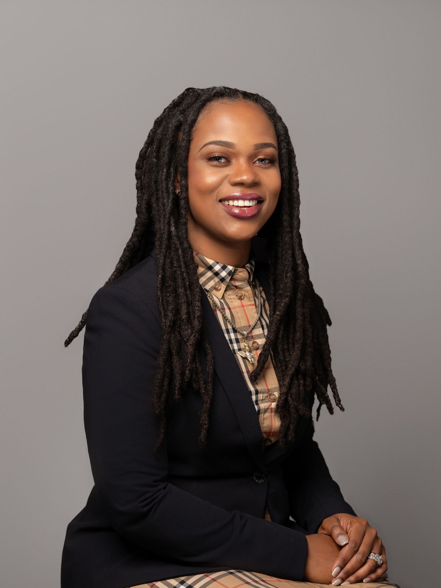 Professional studio portrait featuring dreadlocks, plaid attire and a black cardigan.