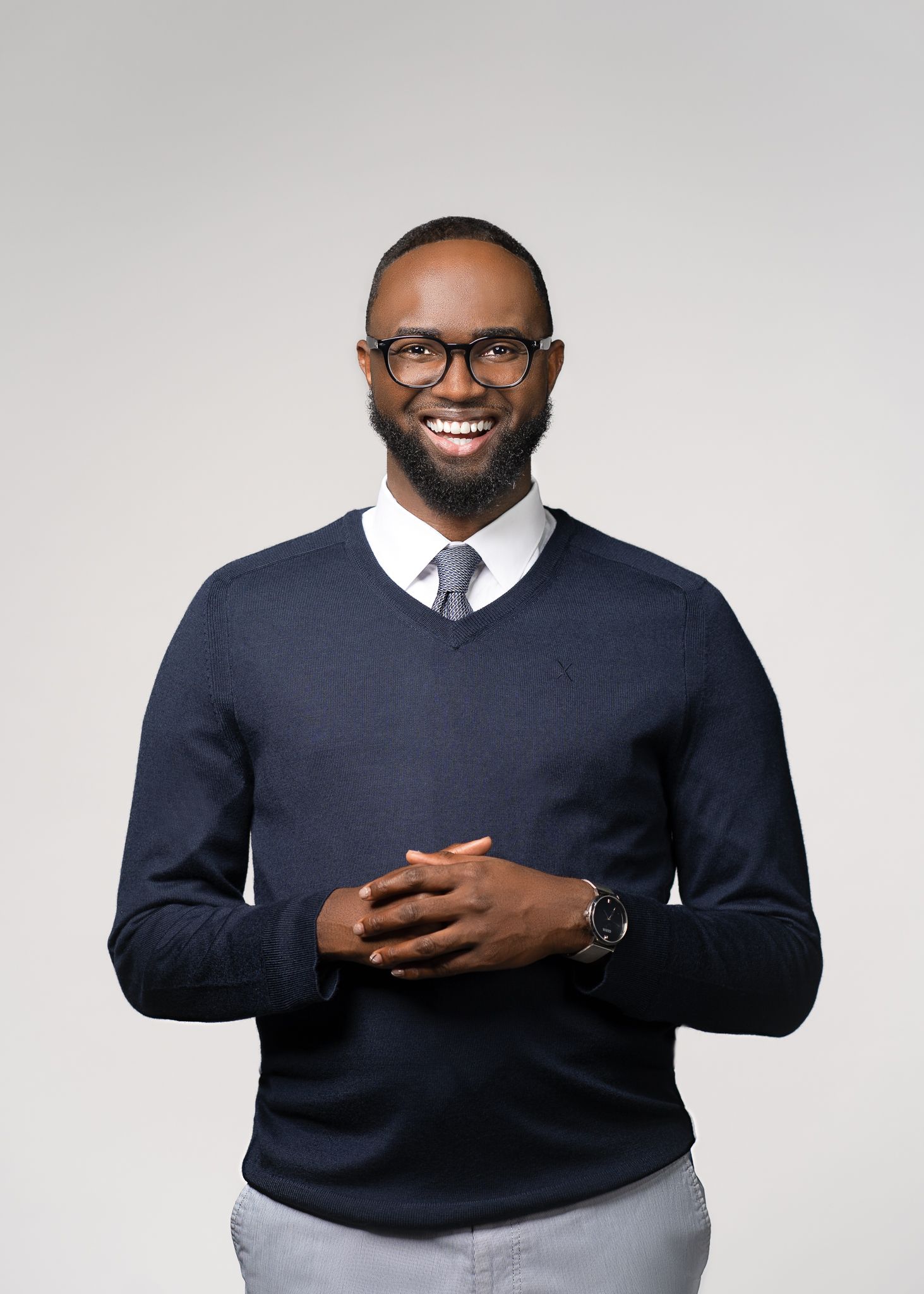 Professional wearing a navy v-neck sweater, white collared shirt and glasses against light background.