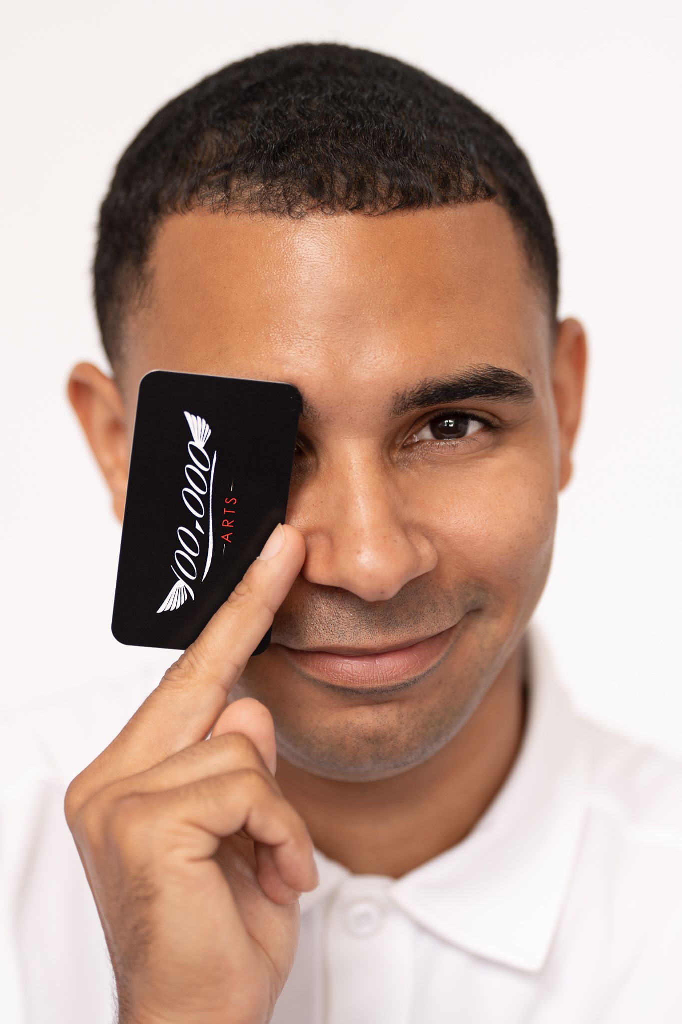 Person in white polo holding black business card next to face against white backdrop.