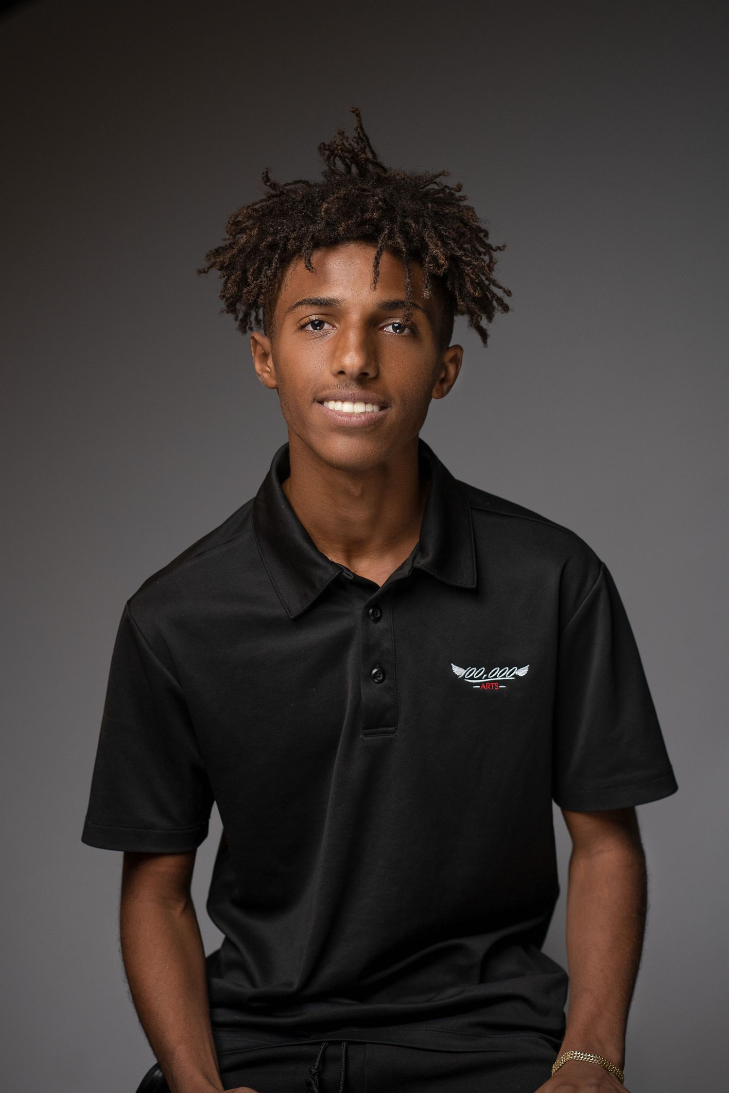 Professional in black polo shirt with company logo against grey studio backdrop.