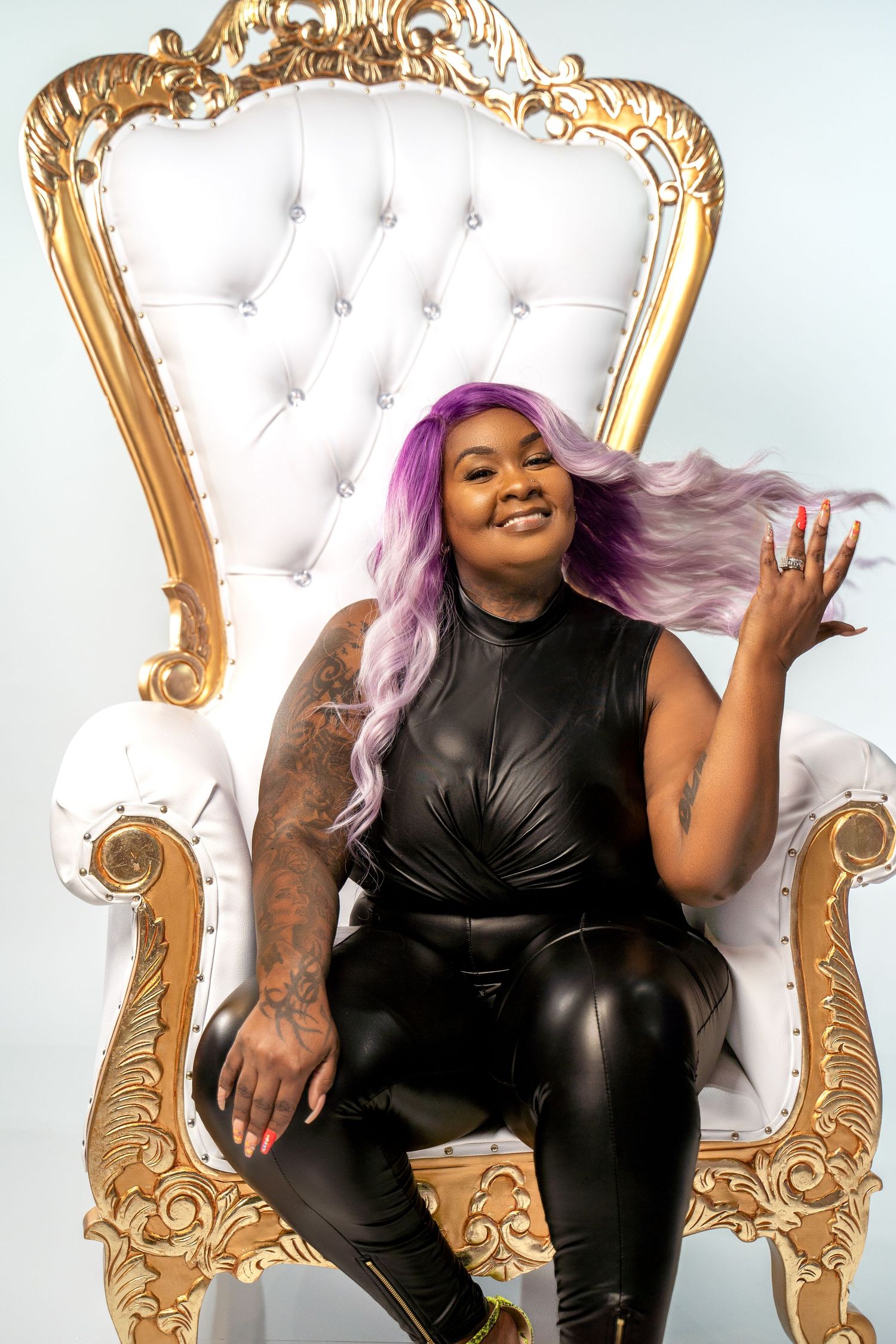 Person with purple hair poses confidently on ornate white and gold throne chair.