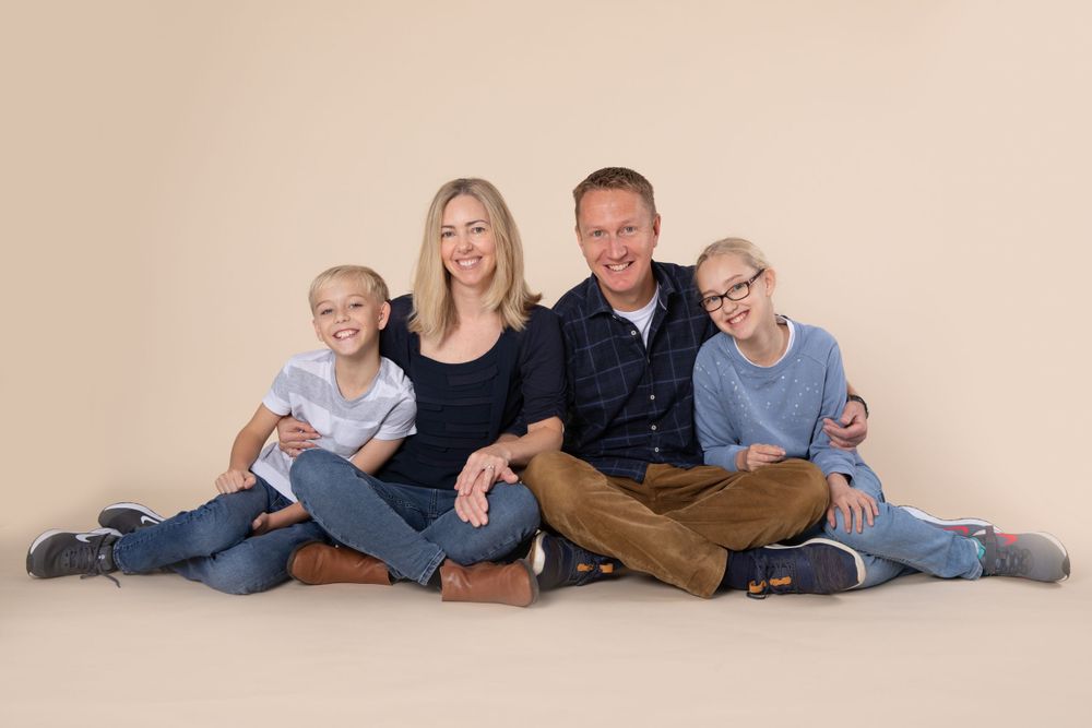 Family portrait of four sitting together against neutral beige background.