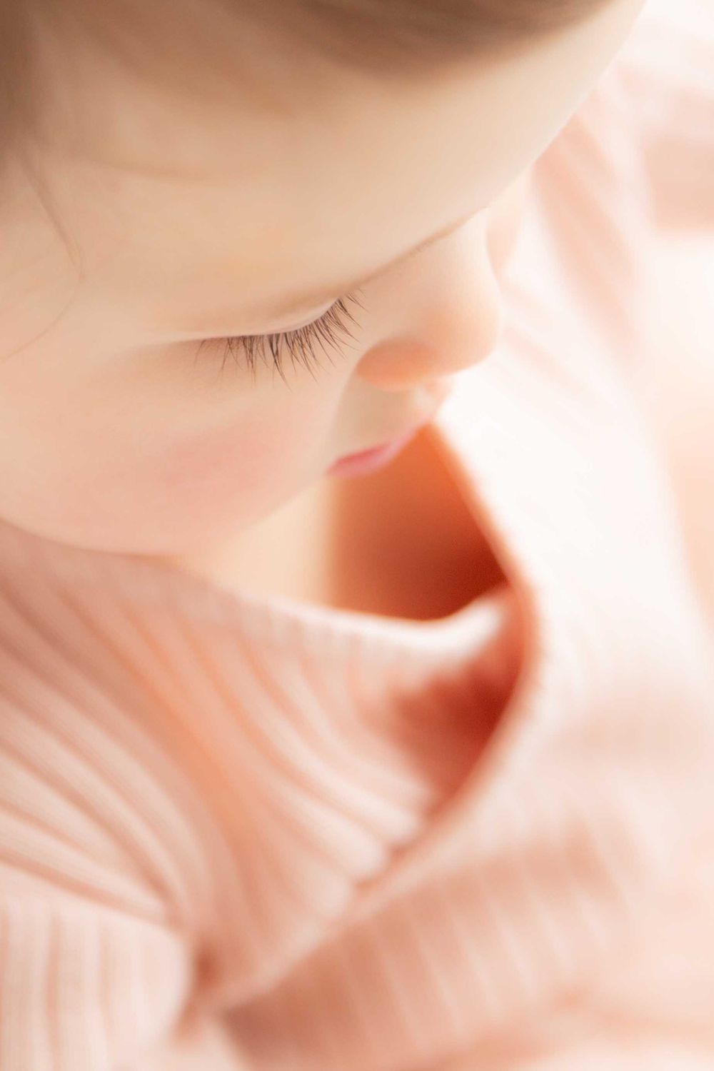 Extreme close-up of baby's eyelashes and profile in soft pink lighting.