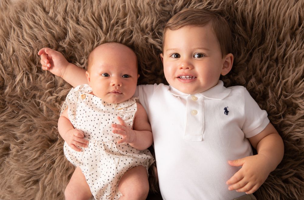Two children lying on brown furry rug during professional photo session.