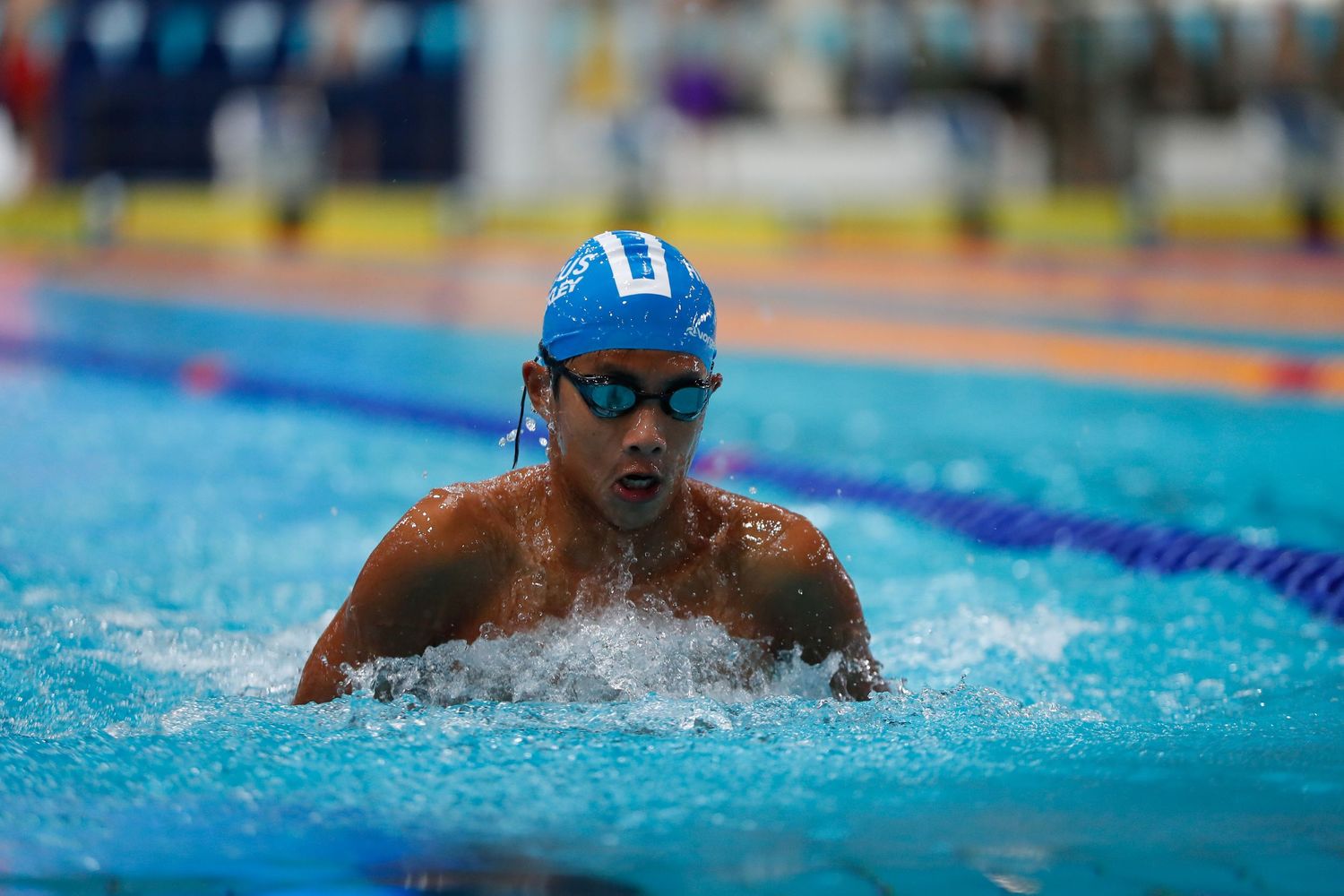 Swimmer in blue cap performing breaststroke during competitive race.