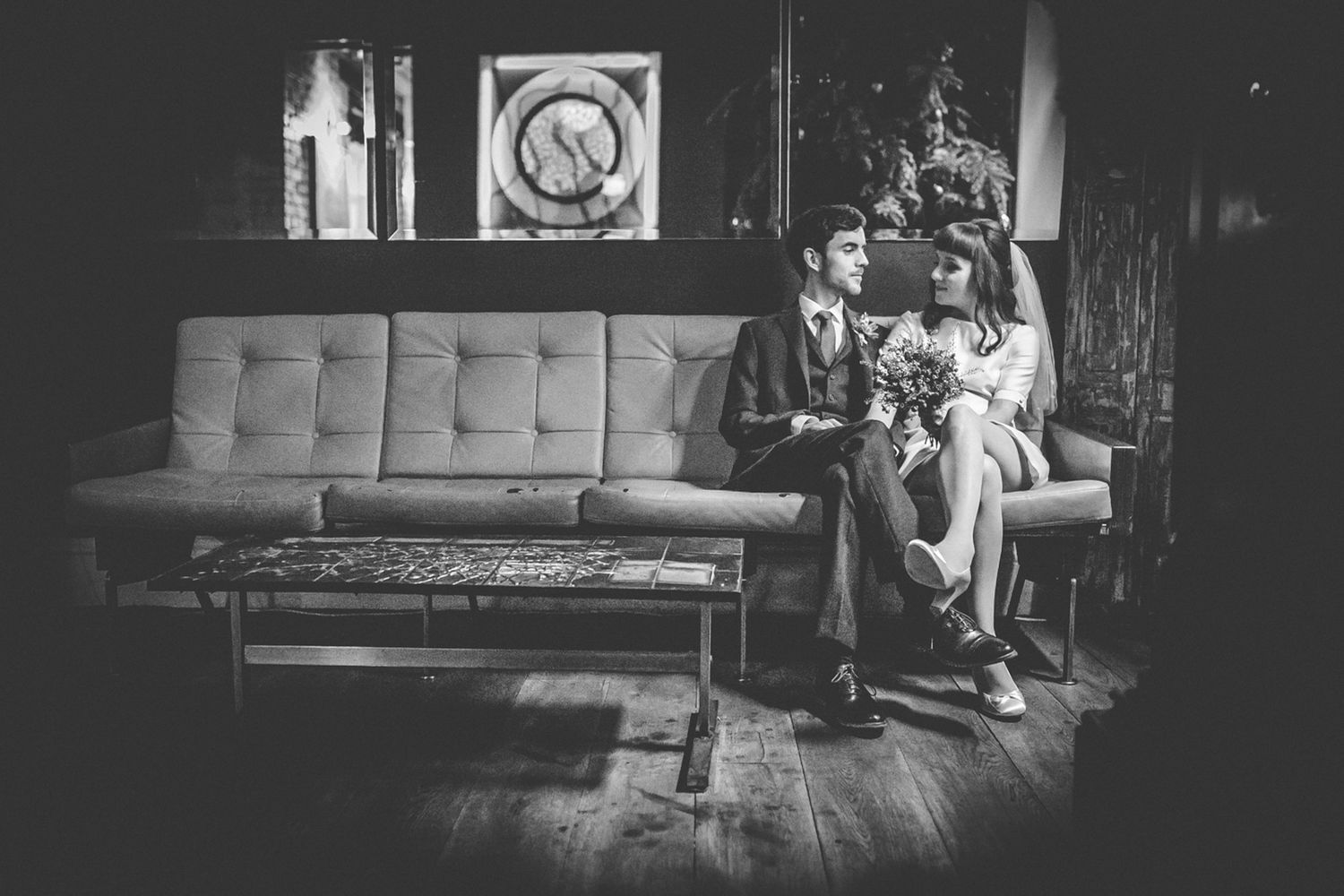 A vintage-style black and white photo of people sitting on a mid-century couch.