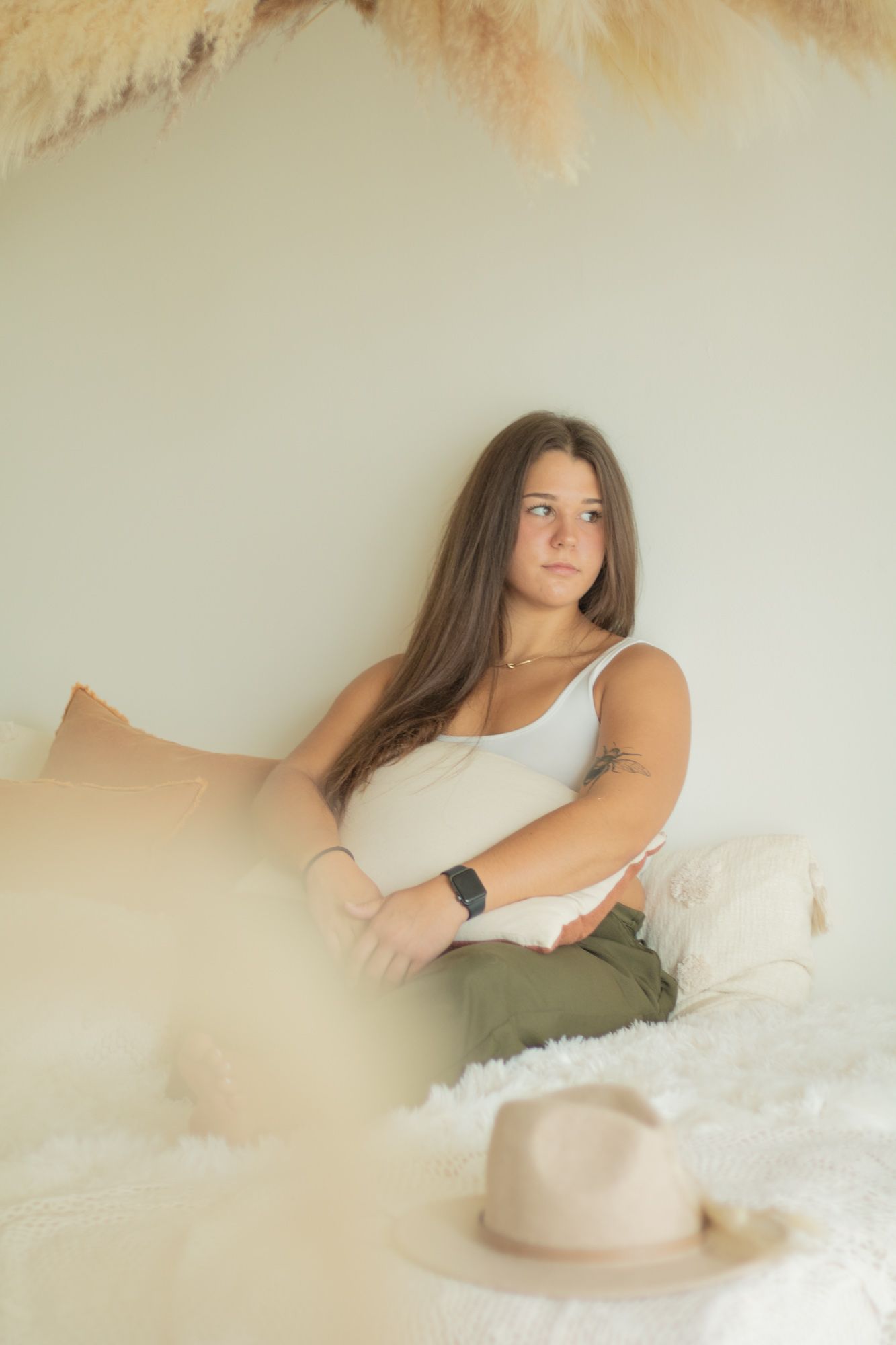 Person relaxing on white bedding with hat nearby in soft ambient lighting.
