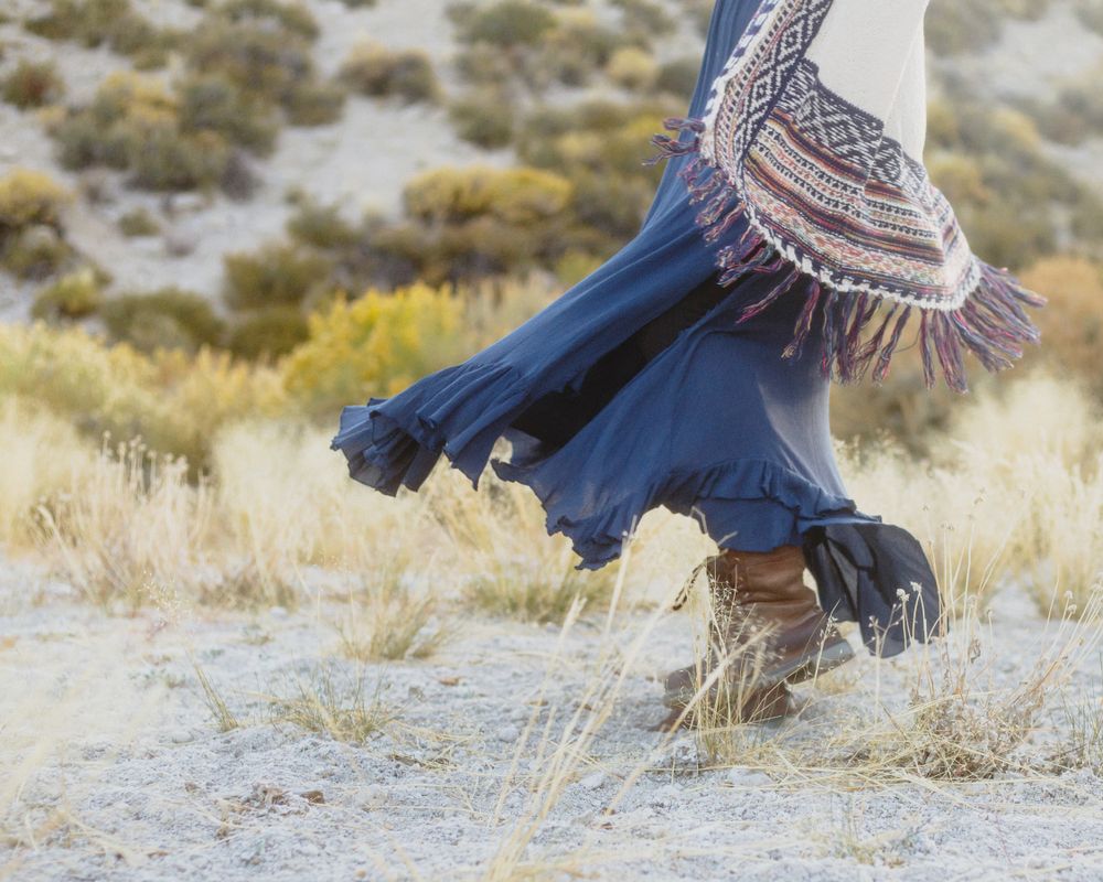 woman's boho dress, sweater, and boots golden hour photography kicking up dust at beach