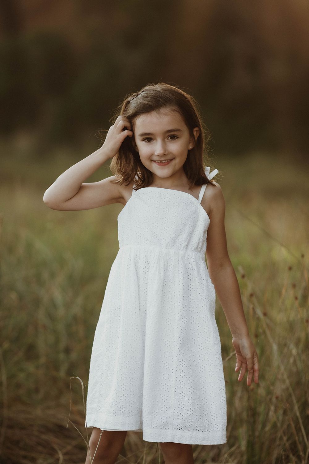 Young girl in white summer dress poses outdoors in natural setting.