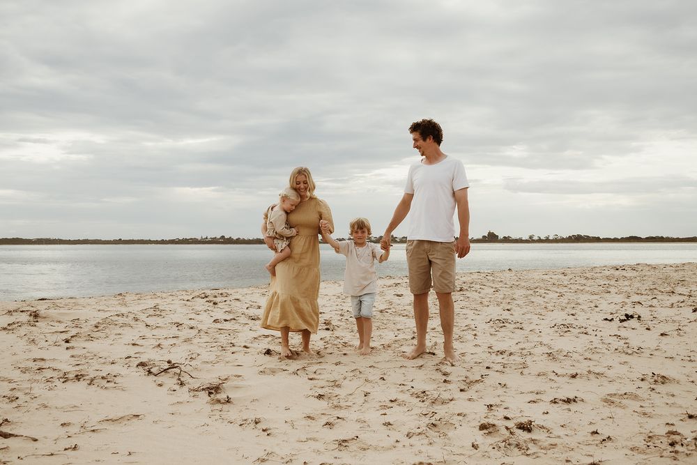 Family walking together on beach under cloudy sky.