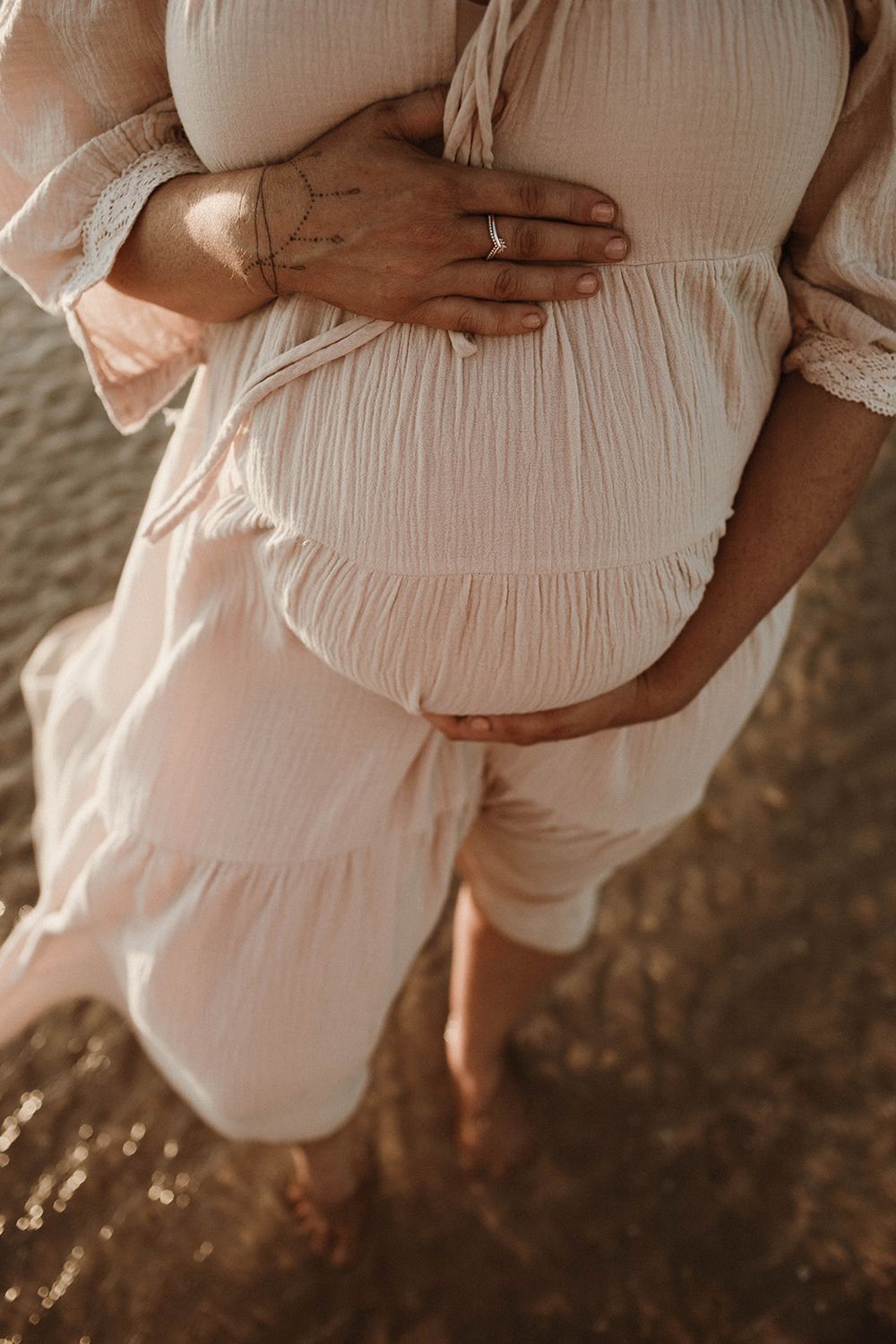 Close-up of hands cradling a pregnant belly in a flowy cream-colored maternity dress.