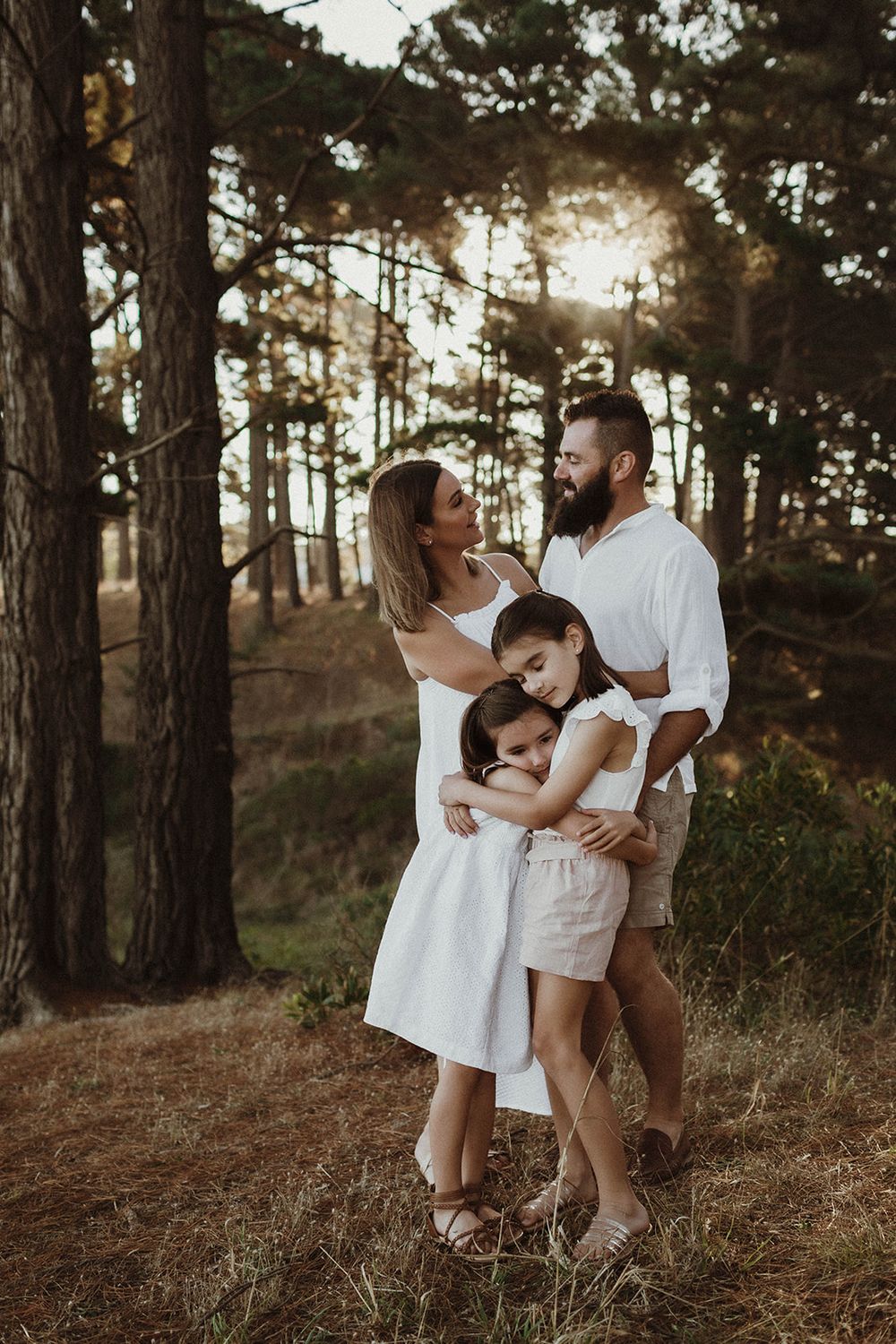A family shares an intimate moment in a forest setting during golden hour.