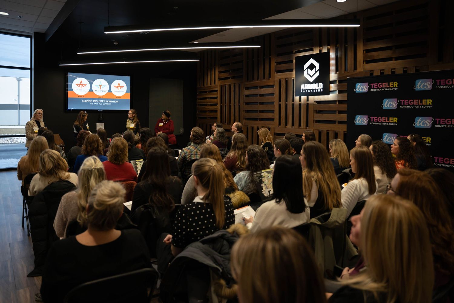 Crowded indoor presentation event with audience members seated in rows.