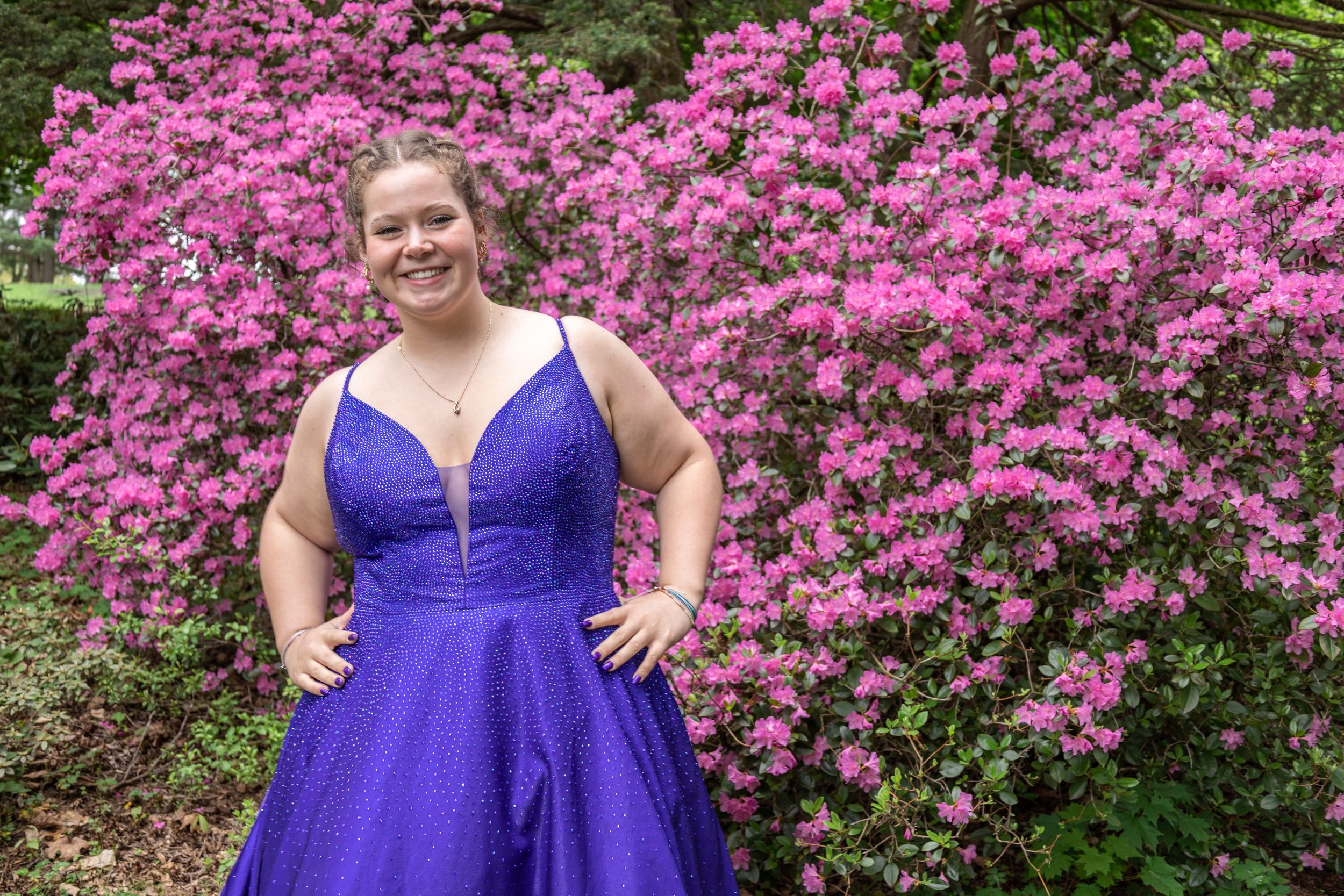 A joyful pose in a deep purple formal gown against vibrant pink azalea blooms.
