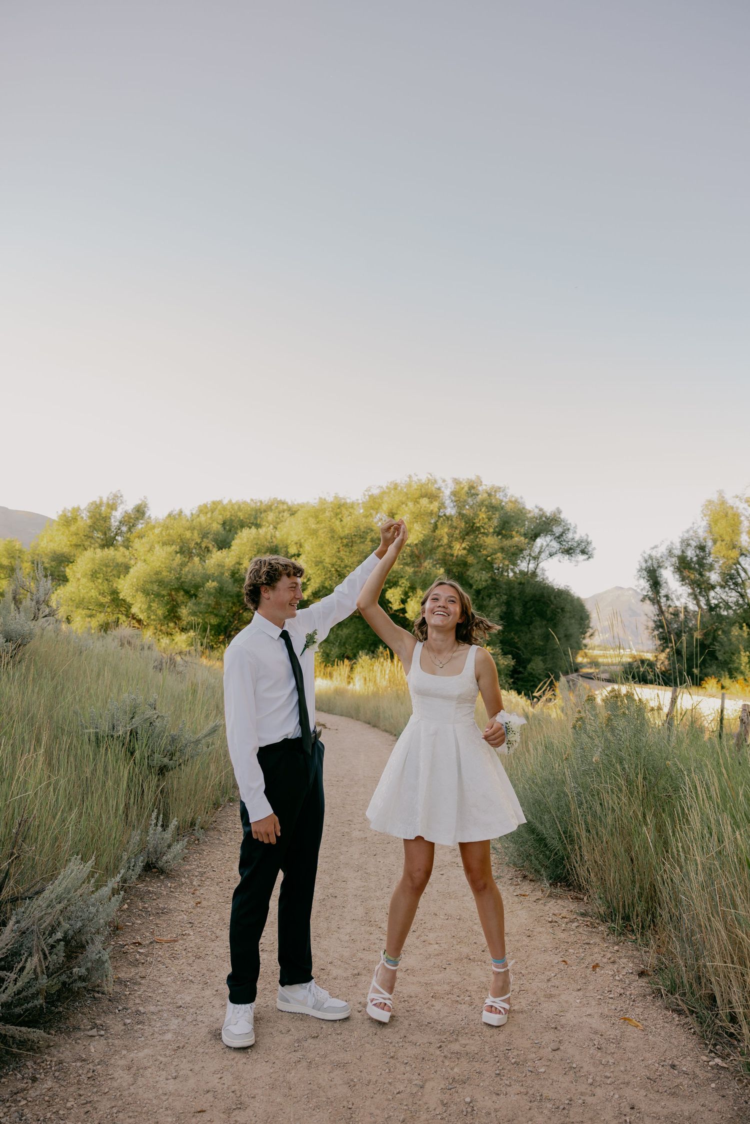 A couple dancing and twirling on a dirt path surrounded by tall grass and trees.