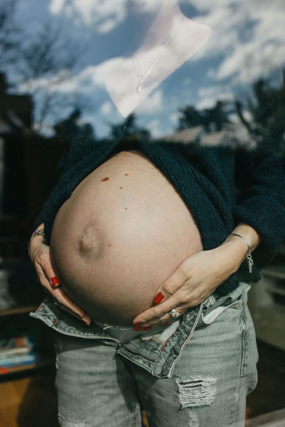 photo du ventre rond d'une future maman en reflet dans une vitre montrant le ciel à Lille pendant une séance grossesse