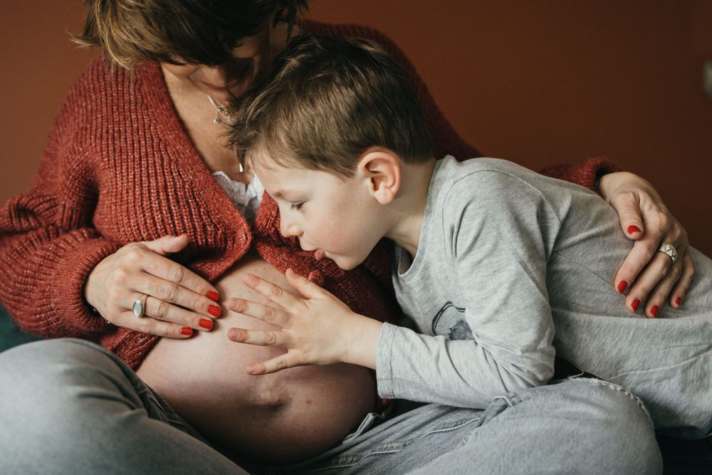 futur grand frère murmurant des mots doux au ventre de sa maman enceinte en séance grossesse à domicile à Lille