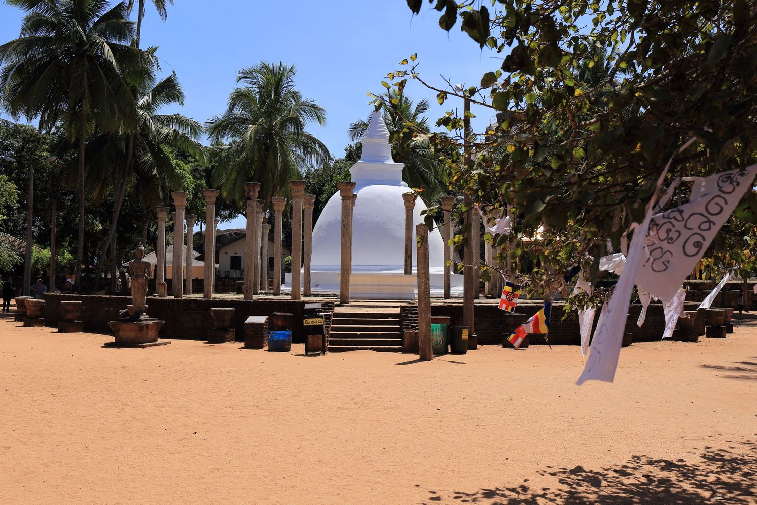 White Buddhist stupa surrounded by palm trees in a sandy courtyard.