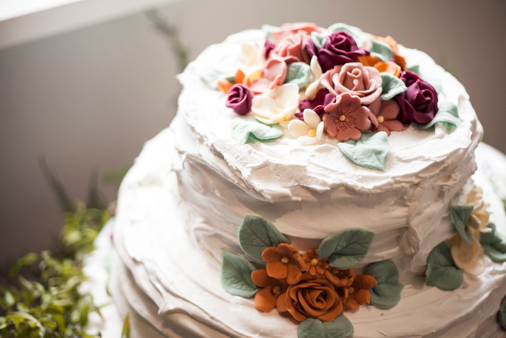 White tiered wedding cake decorated with burgundy and copper roses and eucalyptus.
