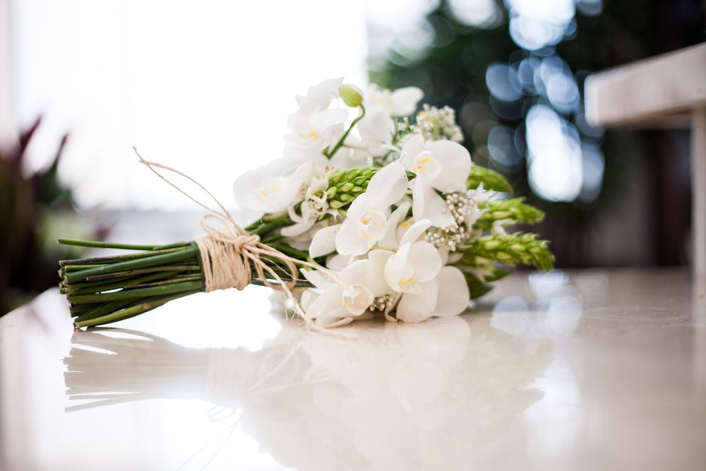 Elegant white floral bouquet tied with twine resting on reflective surface.