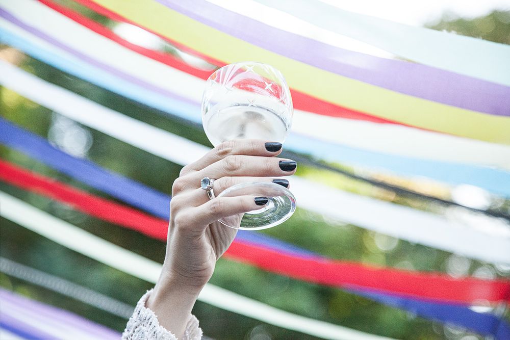 Hand holding a wine glass against colorful streamers in the background.