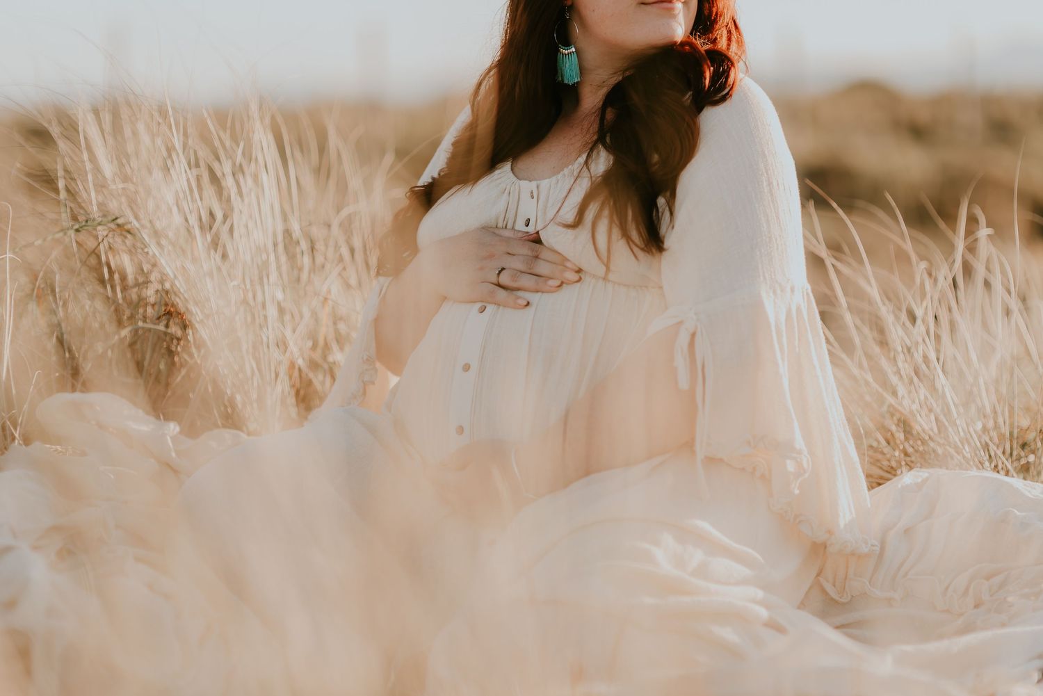 Ethereal maternity portrait in sheer white dress against golden sunset field.