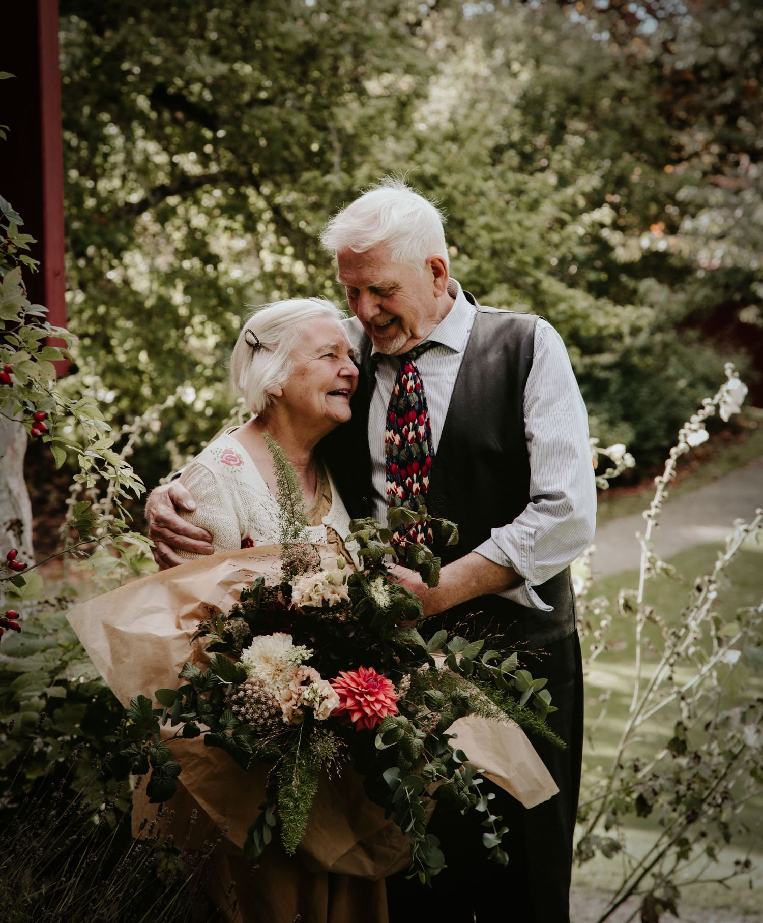 An elderly couple sharing a joyful moment with flowers in a garden setting.