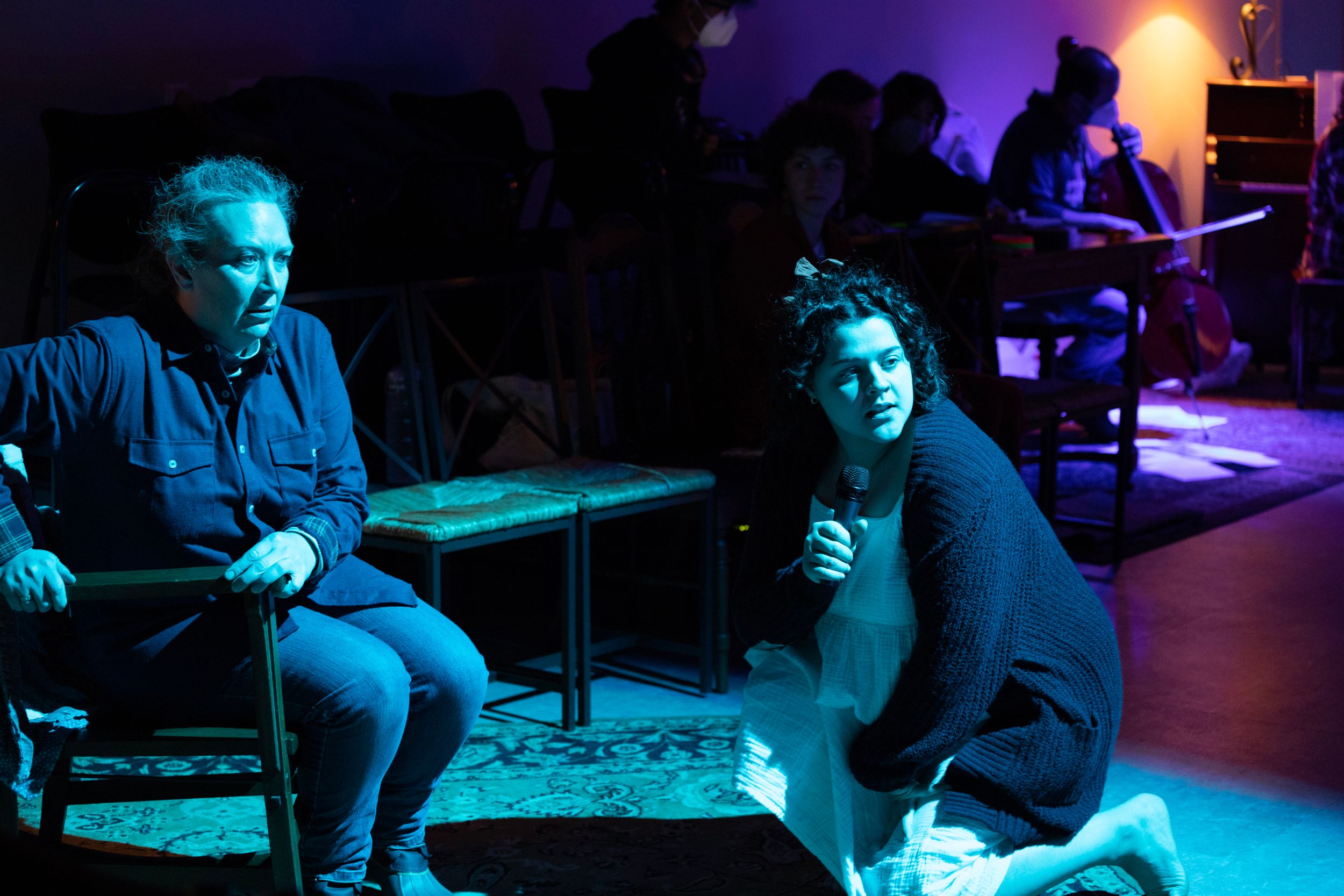 Two performers sit in a dark theater space illuminated by moody blue lighting during a 2022 stage production of Mary's Wondrous Body.