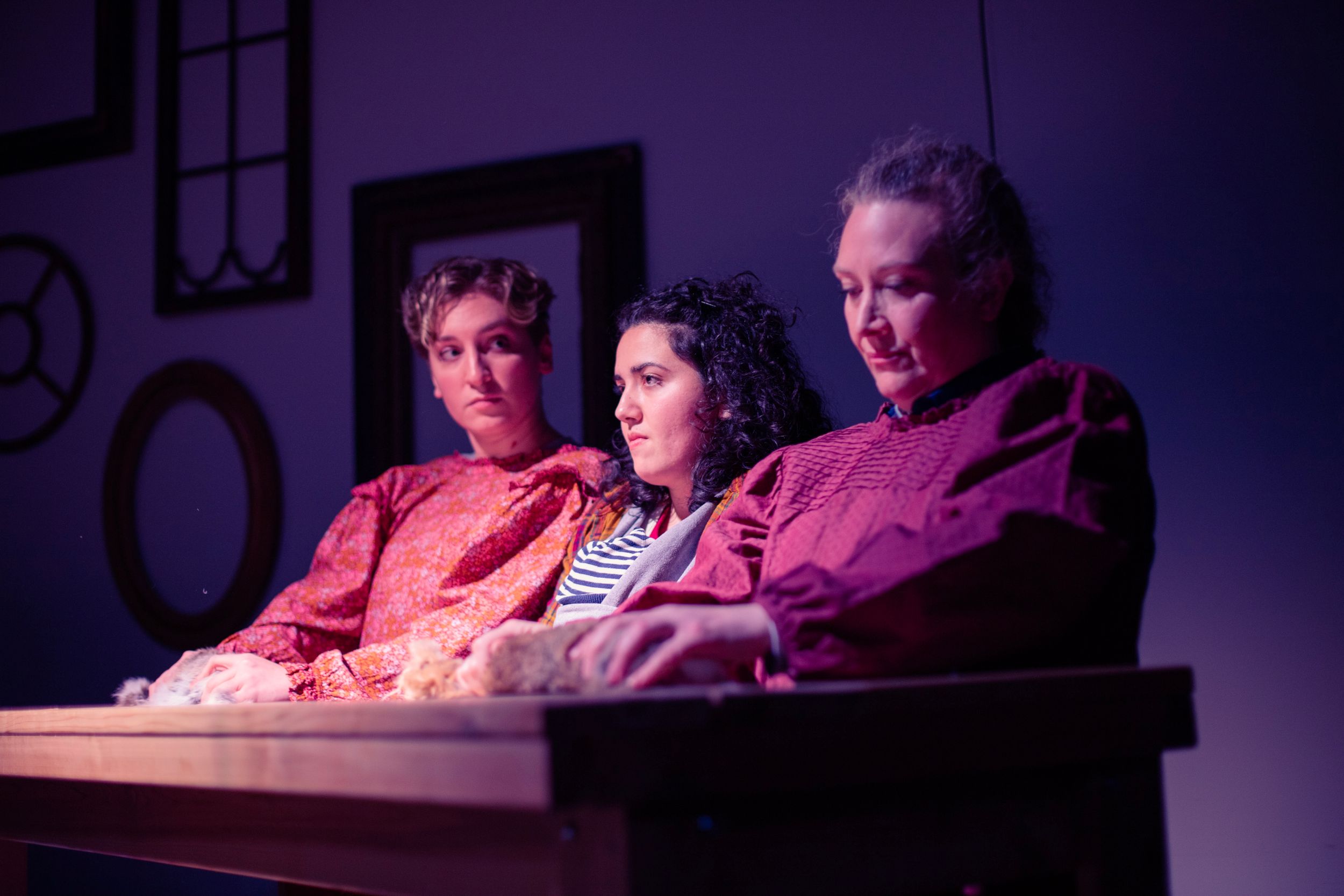 Three actors perform a serious scene in purple theatrical lighting. Production photo from Mary's Wondrous Body in 2022.