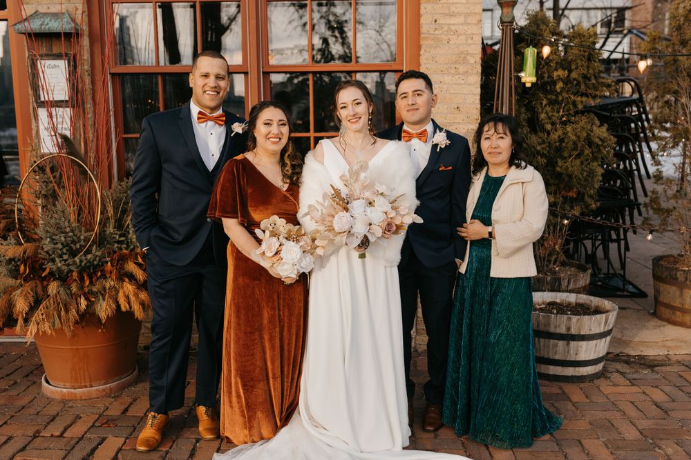 Bride and groom pose with four family members outside decorated venue entrance.