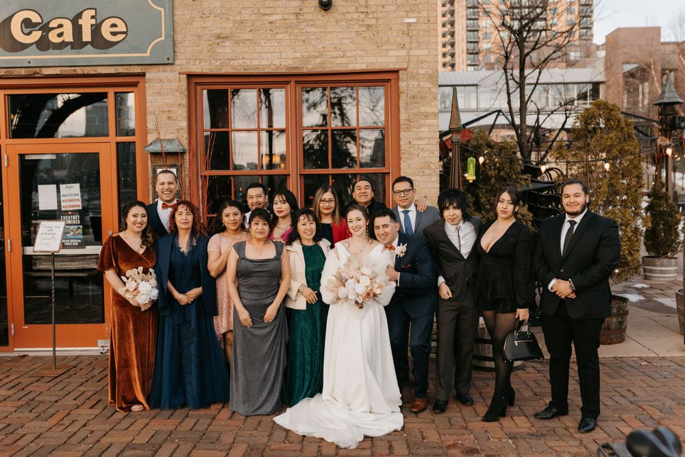 Wedding party poses outside a cafe in winter, bridesmaids in colorful gowns flanking bride and groom.