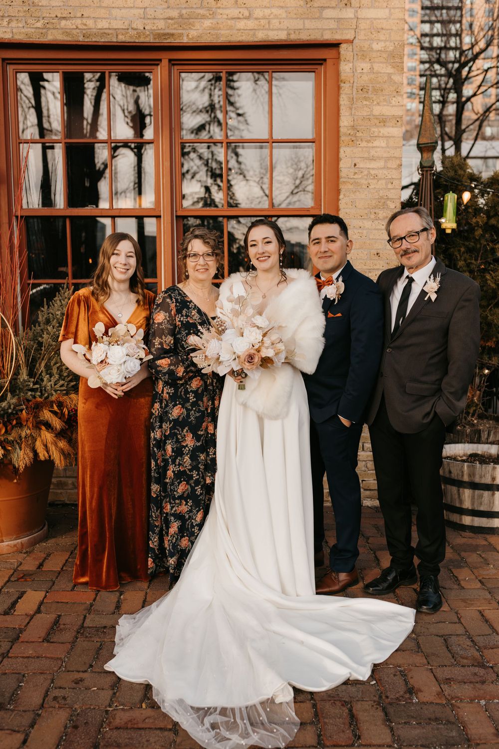 Bride with bouquet poses with family of four outside rustic brick venue.