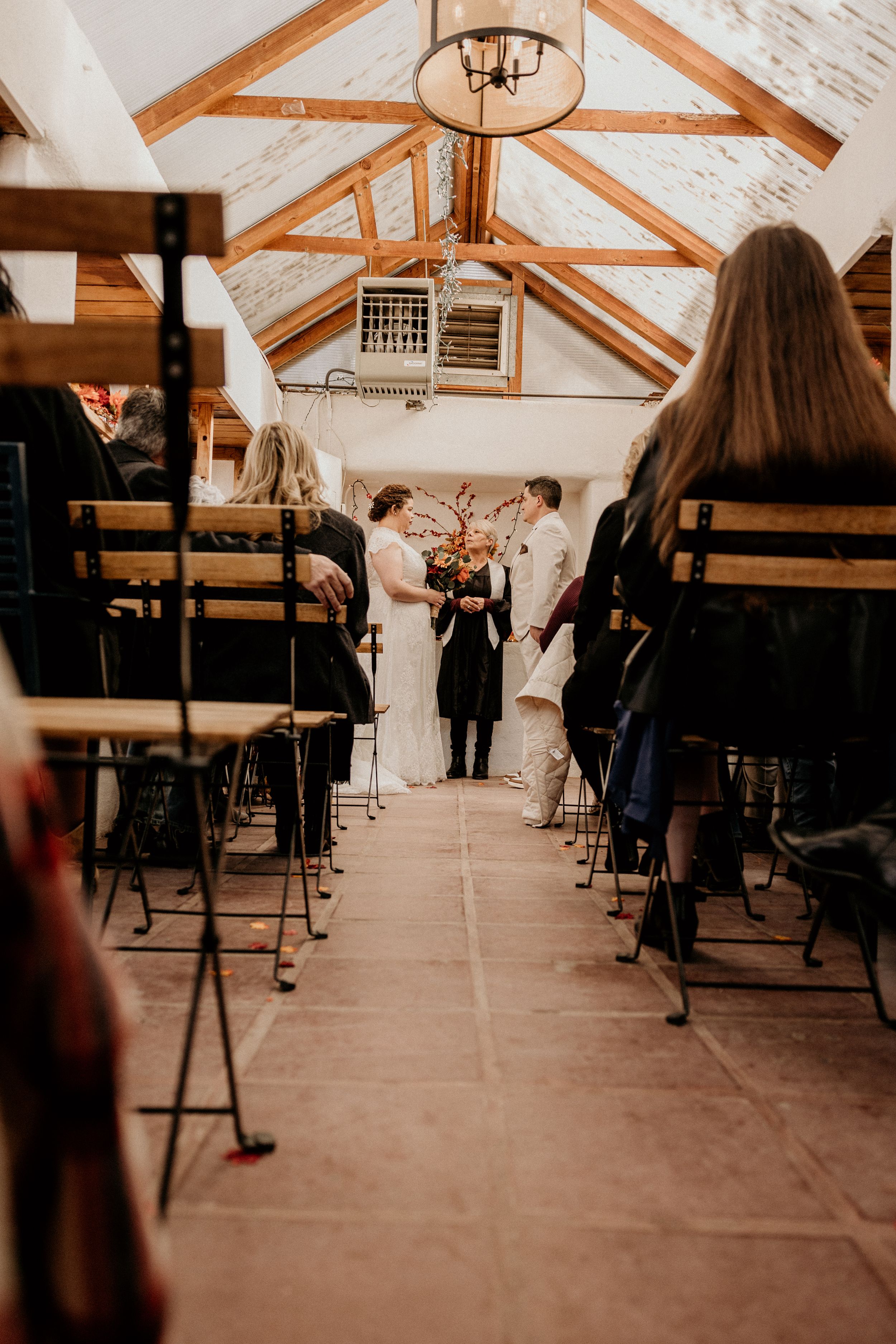 Wedding ceremony in rustic barn venue with vaulted wooden ceiling, guests seated along aisle.