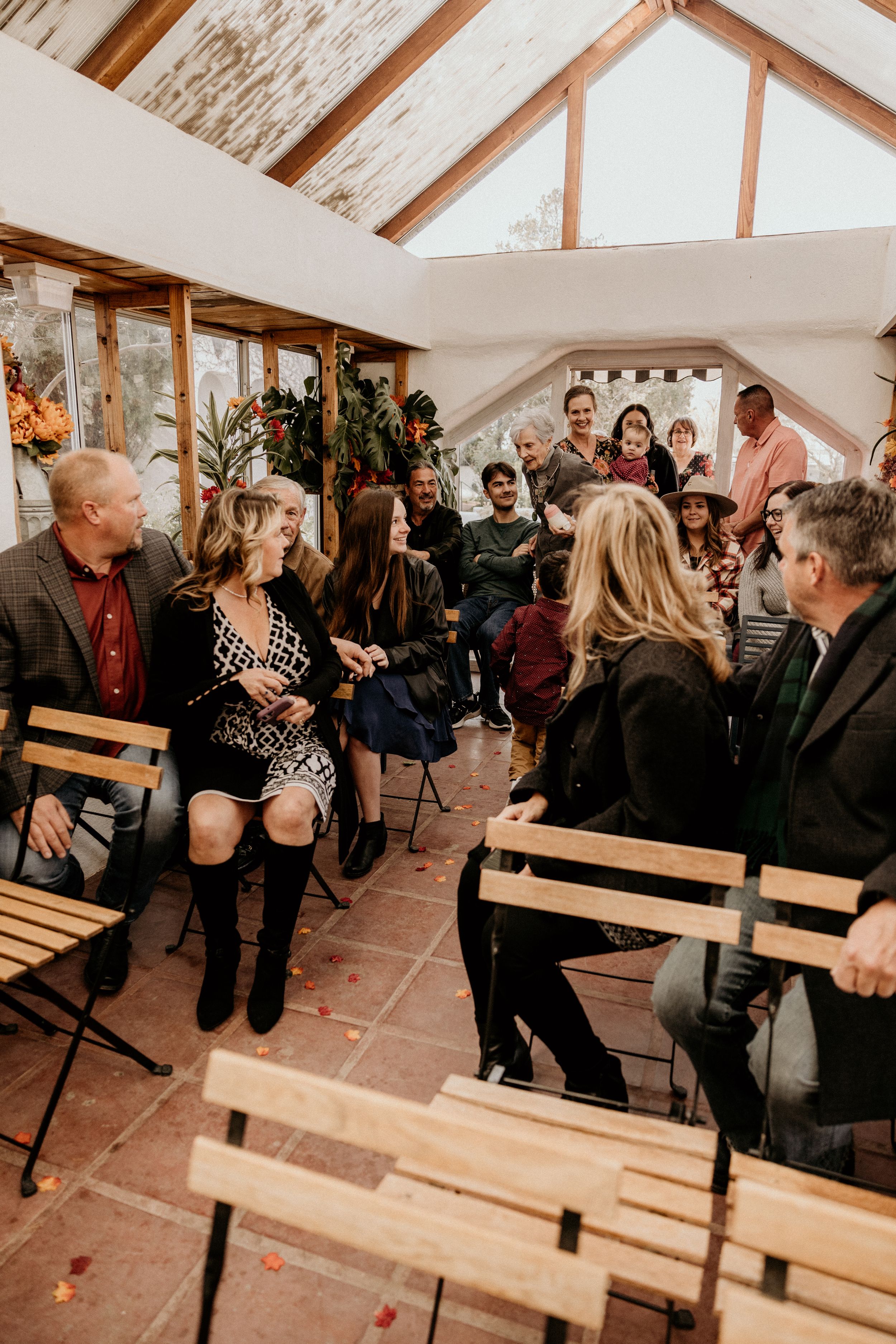 Wedding guests socializing and laughing in rustic barn ceremony venue with wooden beam ceiling.