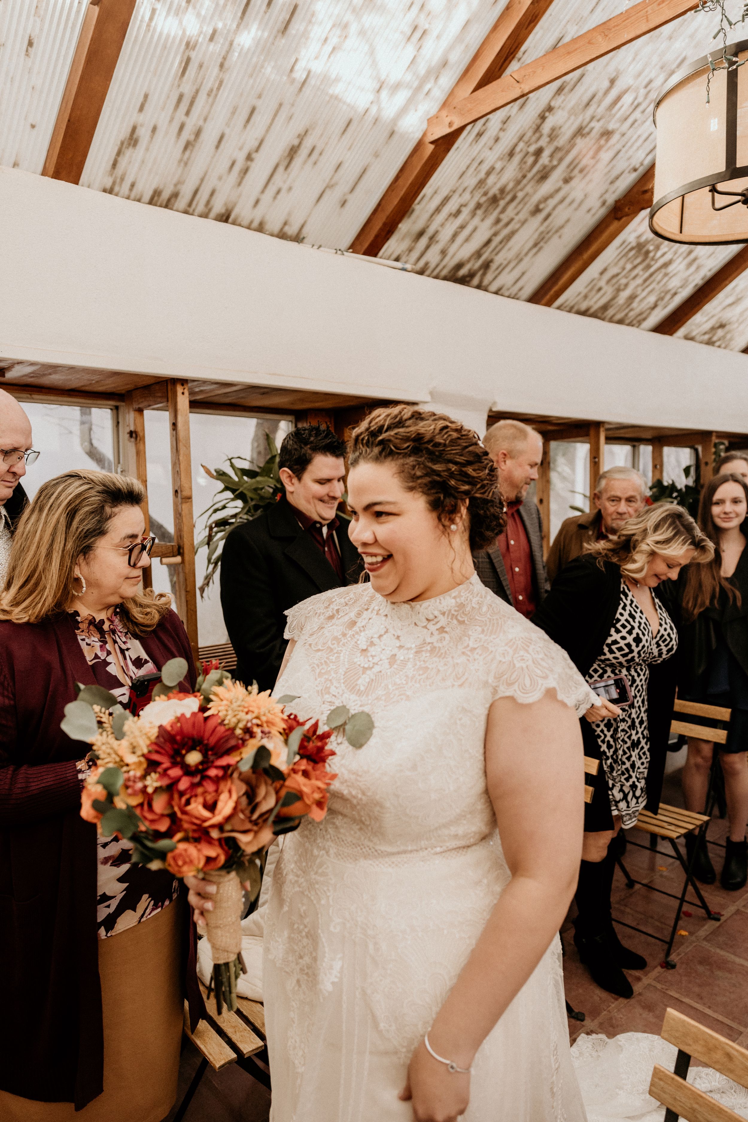 Joyful bride in lace wedding gown laughing while holding autumn bouquet after ceremony.