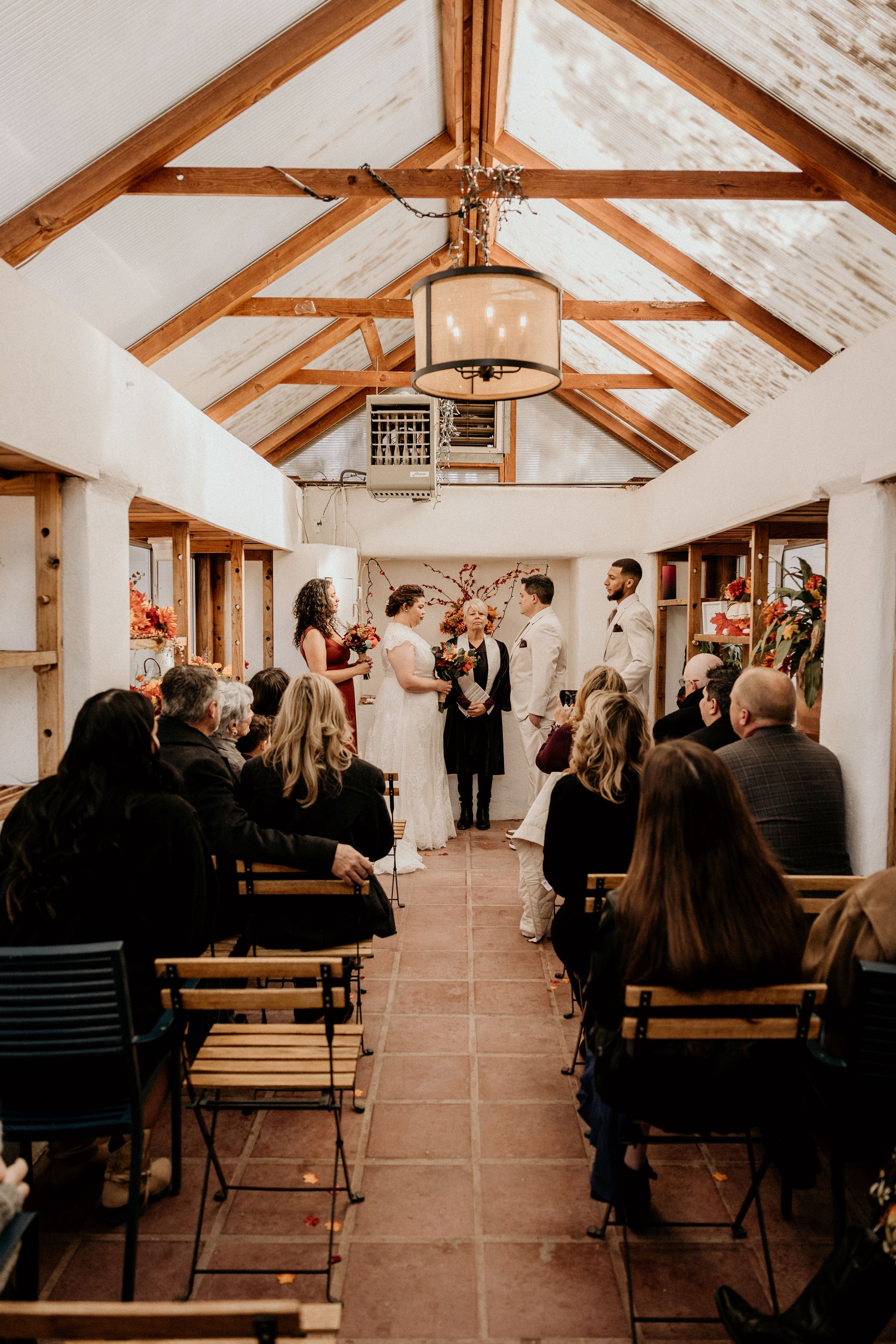 Wedding ceremony in rustic barn with vaulted ceiling, couple at altar surrounded by seated guests.