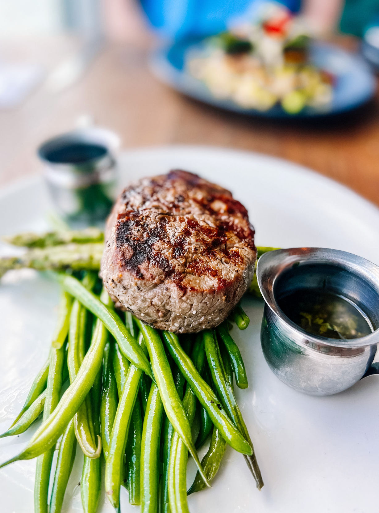 Pan seared steak burger patty served on a bed of fresh steamed green beans in a white ceramic plate.