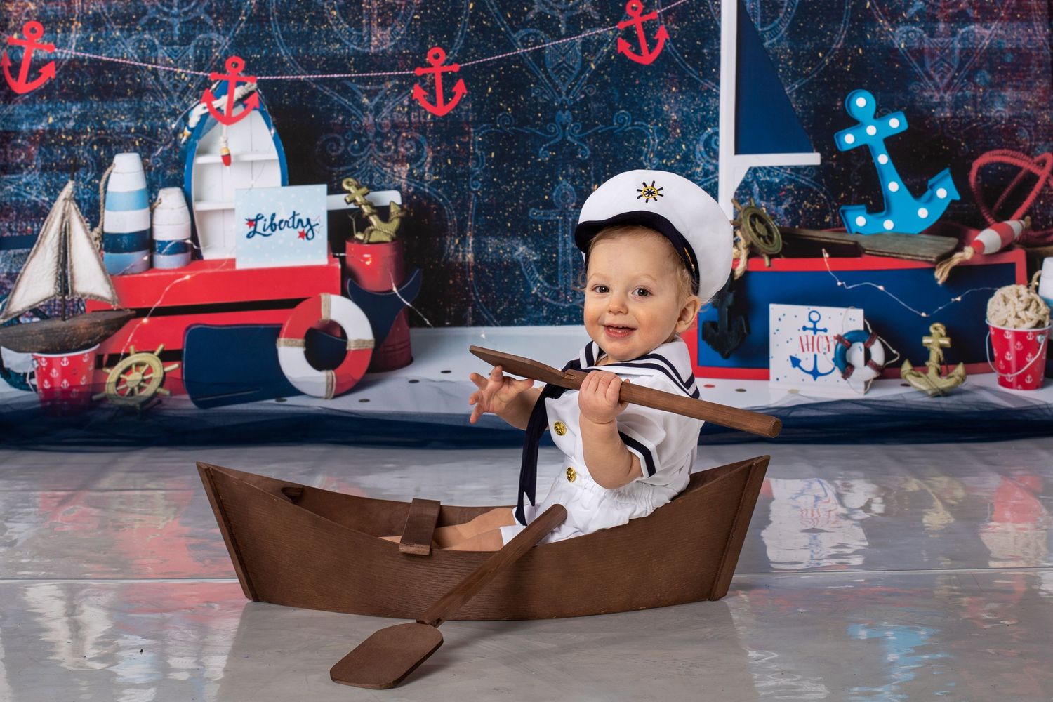 Small wooden boat prop with nautical themed backdrop and decorative anchors.