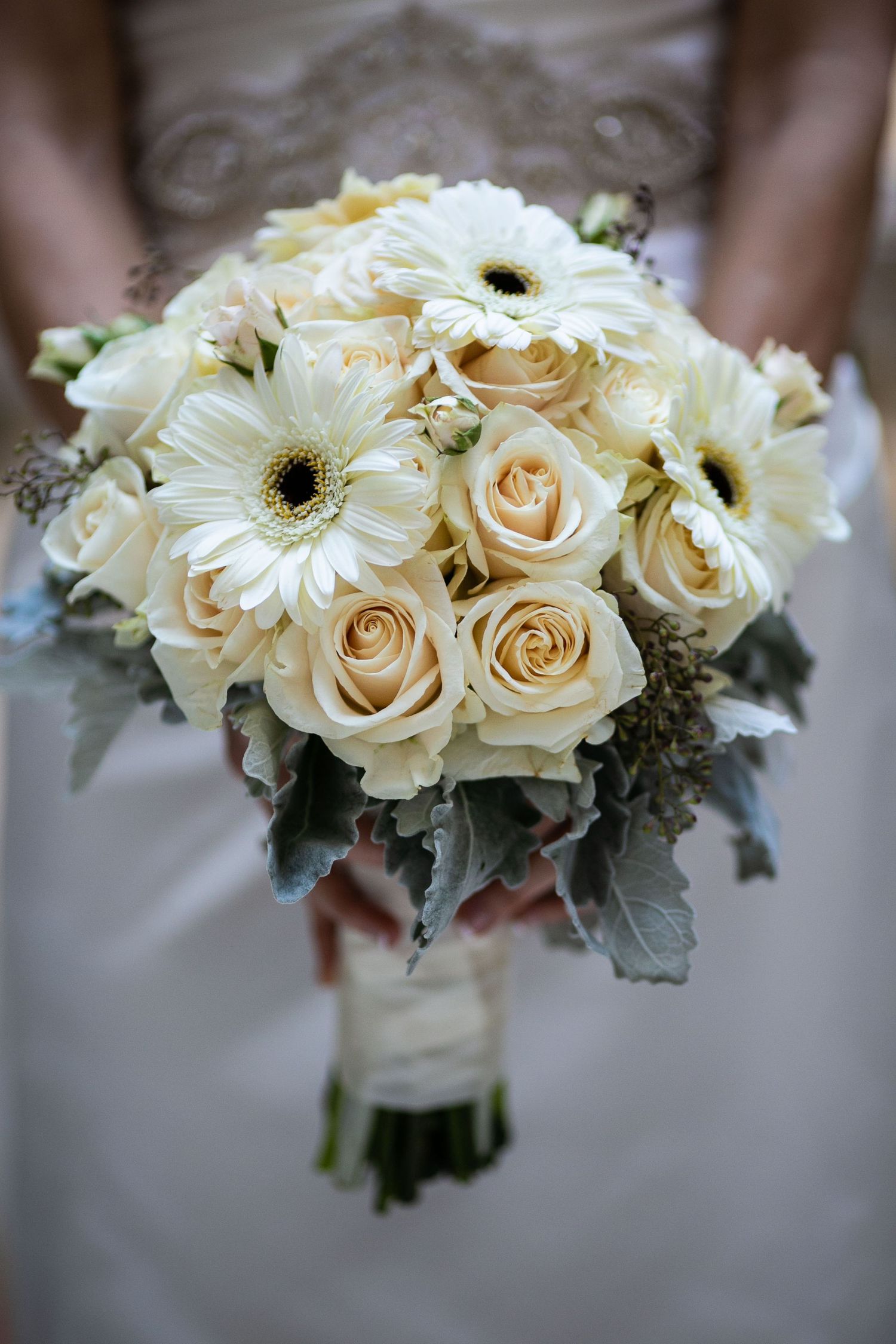A classic white wedding bouquet with roses and gerbera daisies wrapped in ribbon.