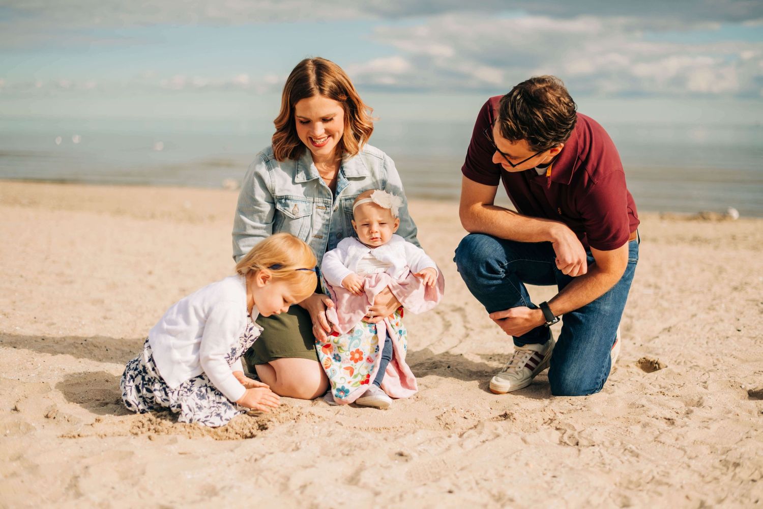mother, father, and two little girls playing in the sand at a beach